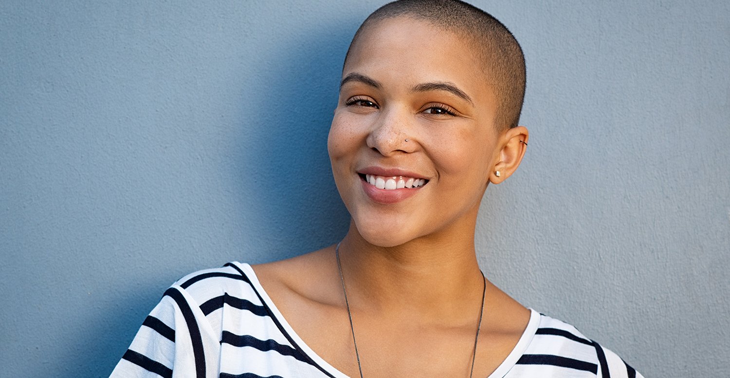 Closeup portrait of beautiful stylish woman on lightblue background. Smiling bald girl looking at camera with copy space. Cheerful and satisfied young woman with shaved head.